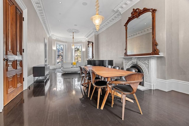dining area with crown molding, a fireplace with raised hearth, baseboards, and dark wood-style floors