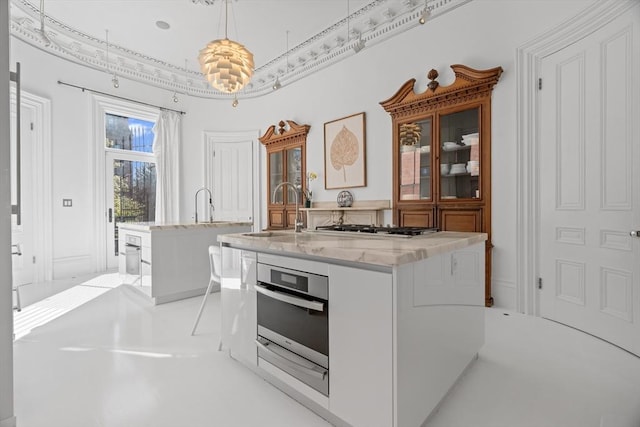 kitchen featuring hanging light fixtures, light stone countertops, a center island with sink, a sink, and stainless steel appliances