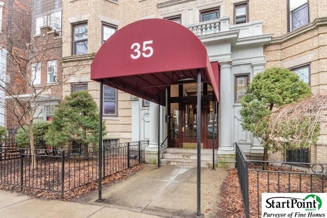 entrance to property featuring fence and brick siding