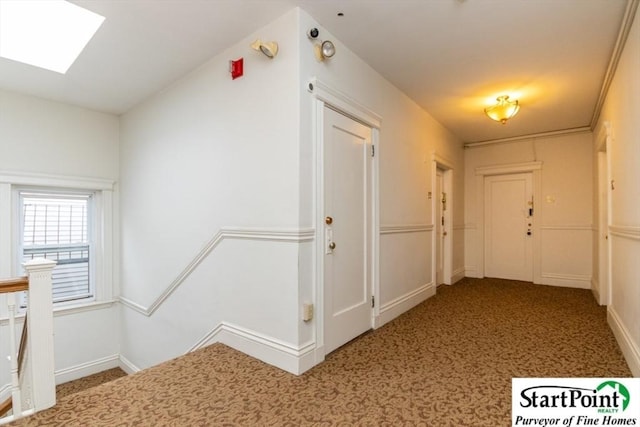 hallway featuring carpet, a skylight, an upstairs landing, and baseboards