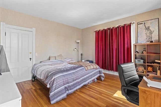 bedroom with wood finished floors, wallpapered walls, and an office area