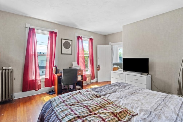 bedroom featuring radiator, wood finished floors, and multiple windows