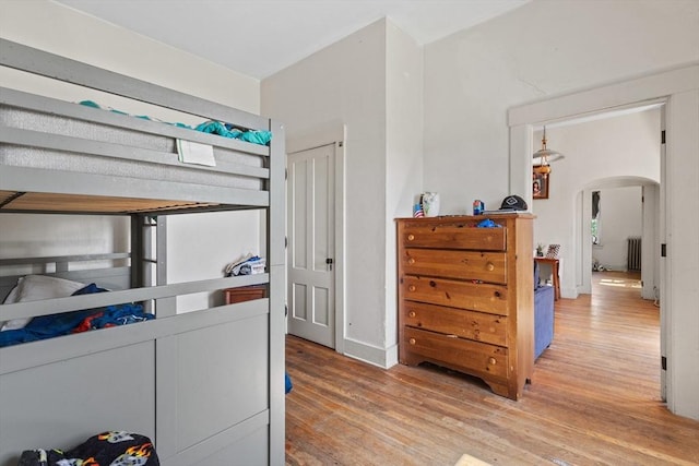 bedroom with arched walkways, wood finished floors, and radiator