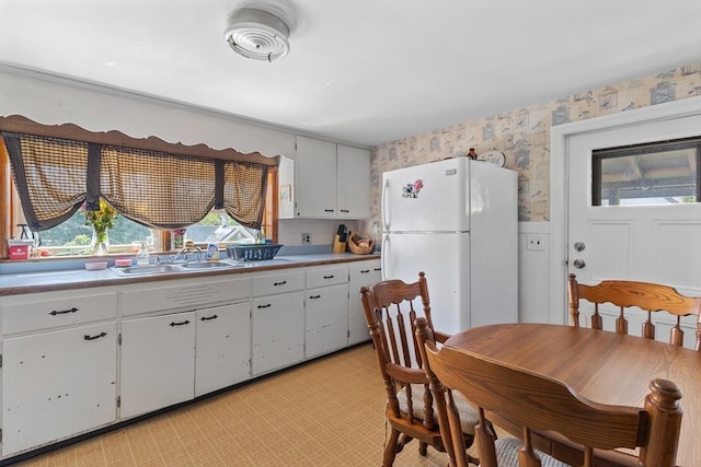 kitchen featuring wallpapered walls, freestanding refrigerator, a sink, white cabinetry, and a wainscoted wall