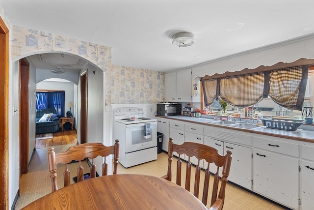 kitchen featuring white electric range, wallpapered walls, black microwave, a sink, and white cabinets