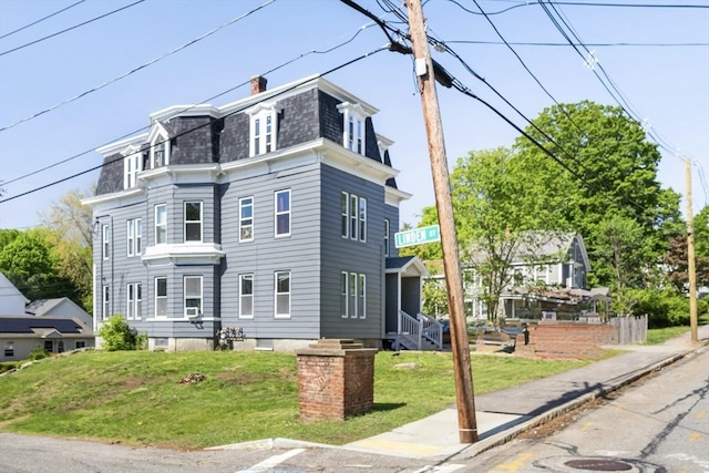 view of front of home with mansard roof, a front lawn, roof with shingles, and a chimney