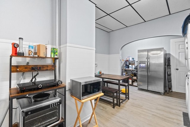 kitchen with appliances with stainless steel finishes, a drop ceiling, light wood-style flooring, and a wainscoted wall