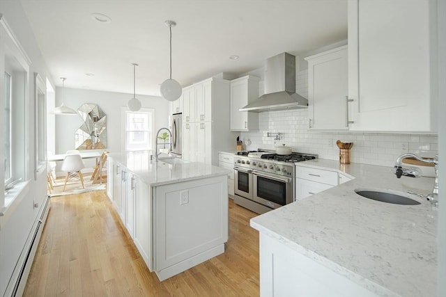 49 Prince St Unit 2, Boston, MA 02130 - kitchen featuring wall chimney range hood, stainless steel appliances, a sink, a baseboard heating unit, and light wood-type flooring