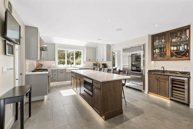 kitchen featuring built in appliances, gray cabinets, beverage cooler, a center island, and wall chimney range hood