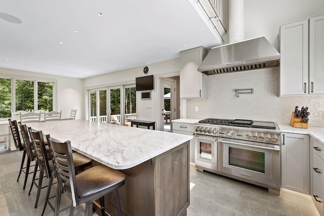 kitchen with a kitchen bar, range with two ovens, a center island, decorative backsplash, and wall chimney range hood