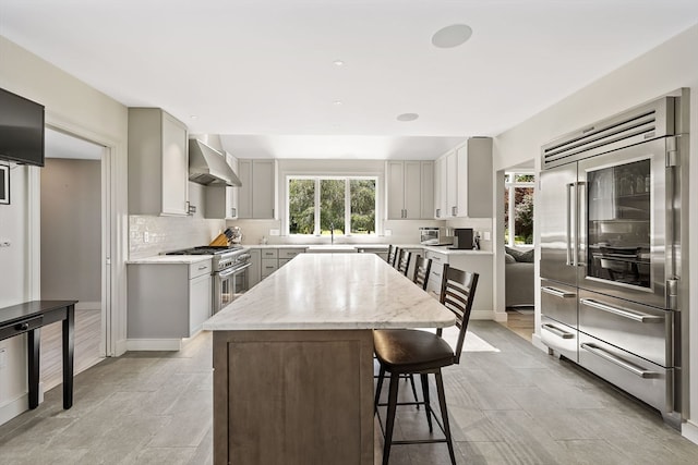 kitchen featuring gray cabinetry, high quality appliances, a kitchen island, and wall chimney exhaust hood