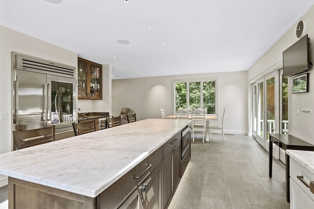 kitchen featuring light stone counters, built in refrigerator, light tile patterned floors, a kitchen island, and dark brown cabinetry