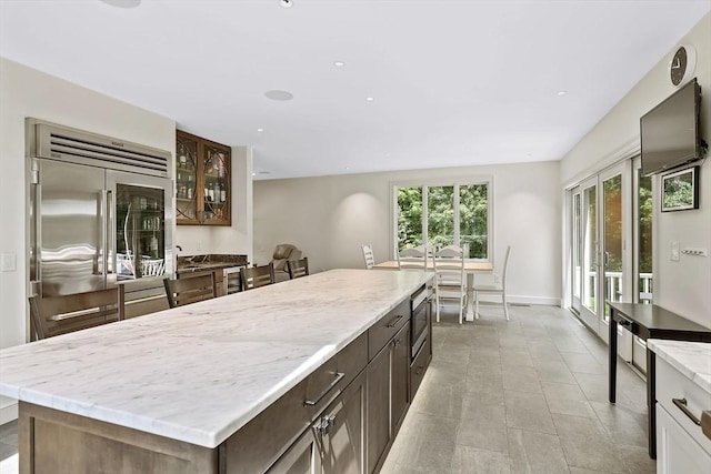 kitchen with light tile patterned flooring, a kitchen island, built in appliances, and dark brown cabinetry