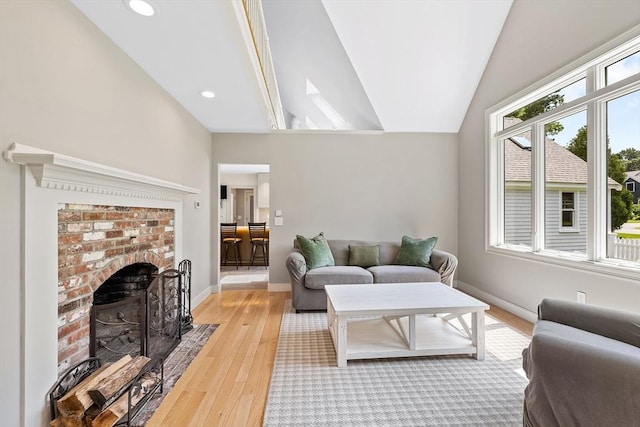 living room featuring a brick fireplace, light hardwood / wood-style floors, and vaulted ceiling with skylight