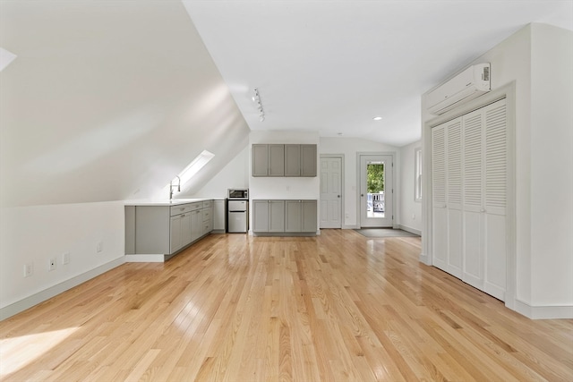 additional living space featuring lofted ceiling, sink, light wood-type flooring, and a wall mounted air conditioner