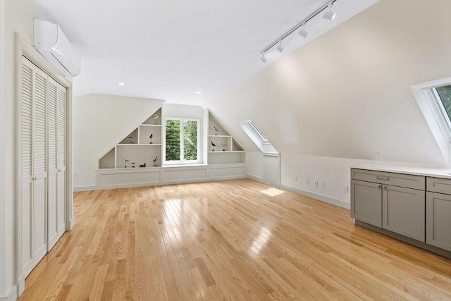 bonus room featuring light hardwood / wood-style flooring, vaulted ceiling with skylight, a wall unit AC, and built in shelves