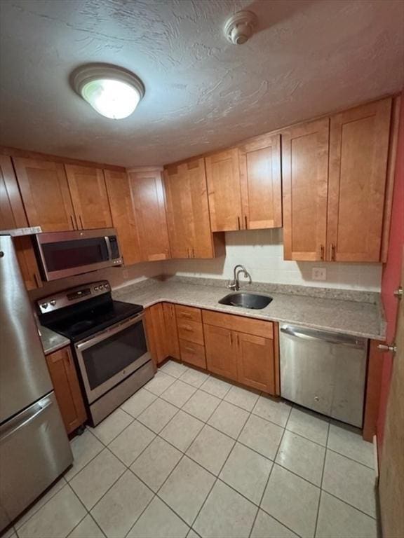 kitchen with brown cabinets, stainless steel appliances, light countertops, light tile patterned flooring, and a sink