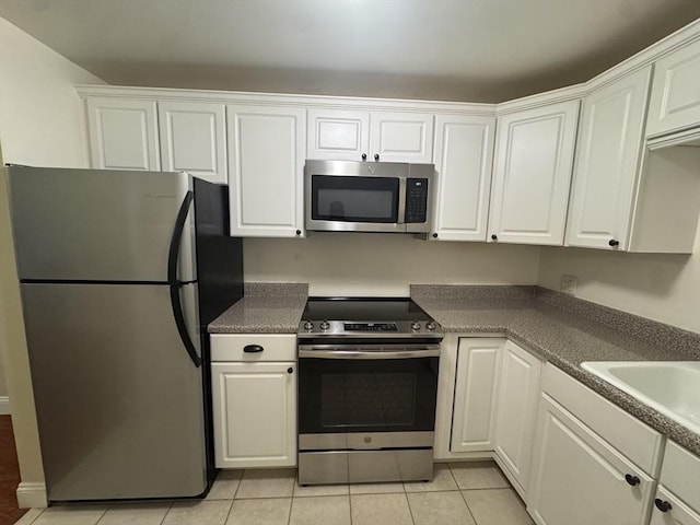 kitchen with appliances with stainless steel finishes, white cabinetry, light tile patterned flooring, and sink