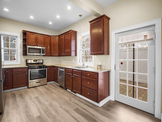 kitchen featuring pendant lighting, appliances with stainless steel finishes, light wood-style floors, a sink, and light stone countertops