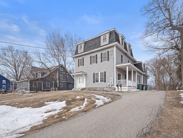 second empire-style home with aphalt driveway, mansard roof, a porch, and a shingled roof