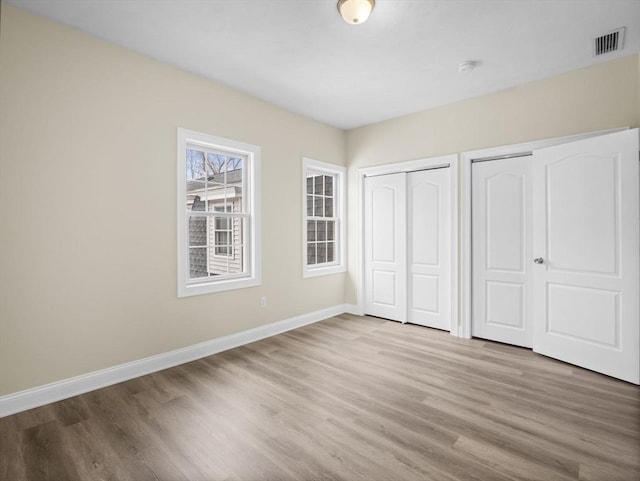 unfurnished bedroom featuring multiple closets, visible vents, baseboards, and wood finished floors