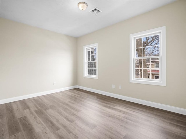 empty room featuring visible vents, baseboards, and wood finished floors