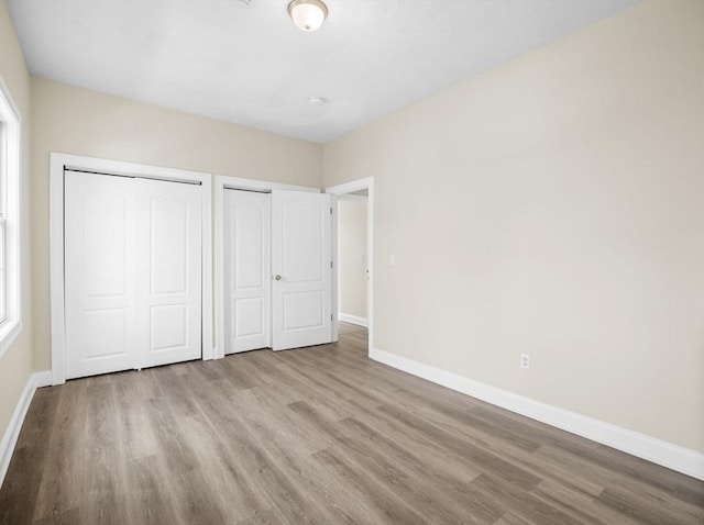 unfurnished bedroom featuring multiple closets, multiple windows, baseboards, and wood finished floors