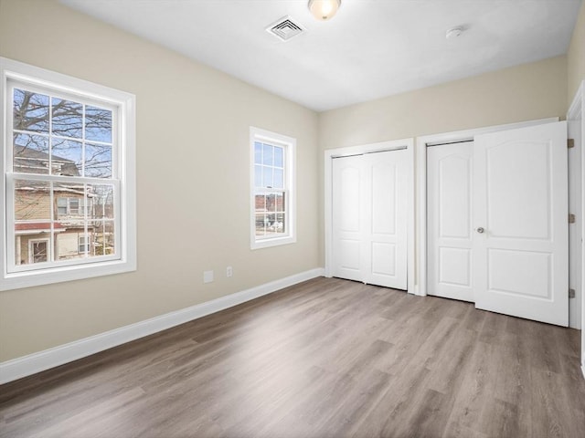 unfurnished bedroom with multiple closets, visible vents, baseboards, and wood finished floors