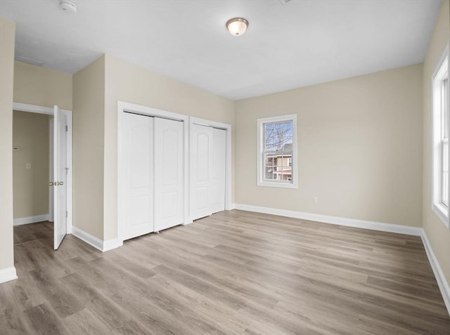 unfurnished bedroom with wood finished floors, two closets, and baseboards