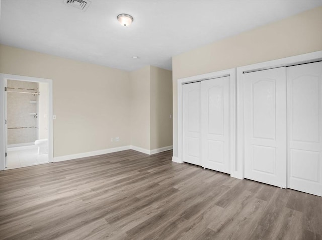 unfurnished bedroom with two closets, visible vents, connected bathroom, wood finished floors, and baseboards