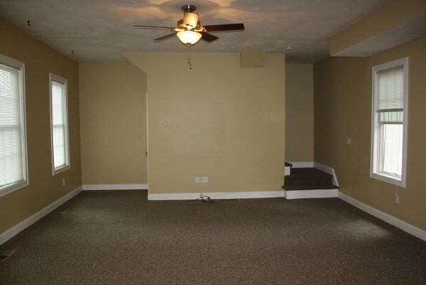 empty room featuring ceiling fan, baseboards, dark carpet, and a textured ceiling