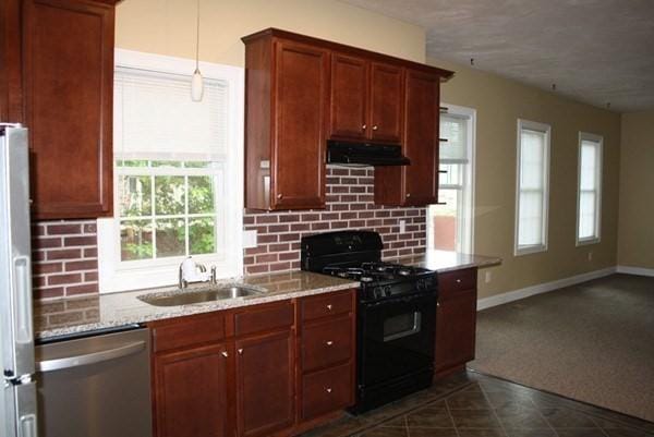 kitchen with appliances with stainless steel finishes, a sink, light stone countertops, under cabinet range hood, and backsplash