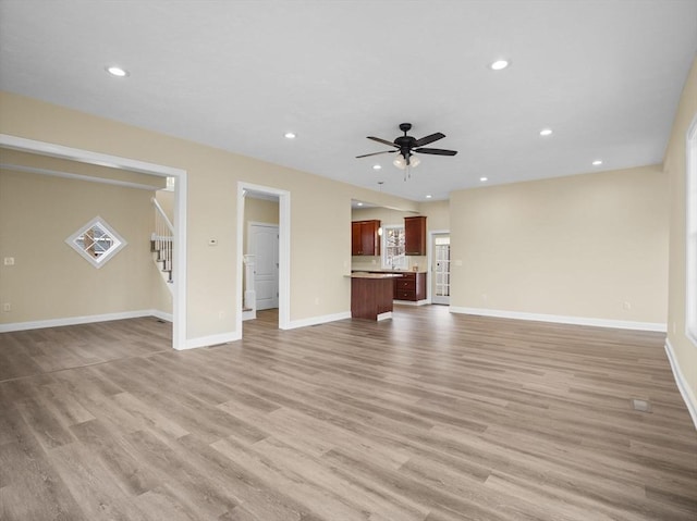 unfurnished living room featuring a ceiling fan, recessed lighting, light wood-style flooring, and stairs