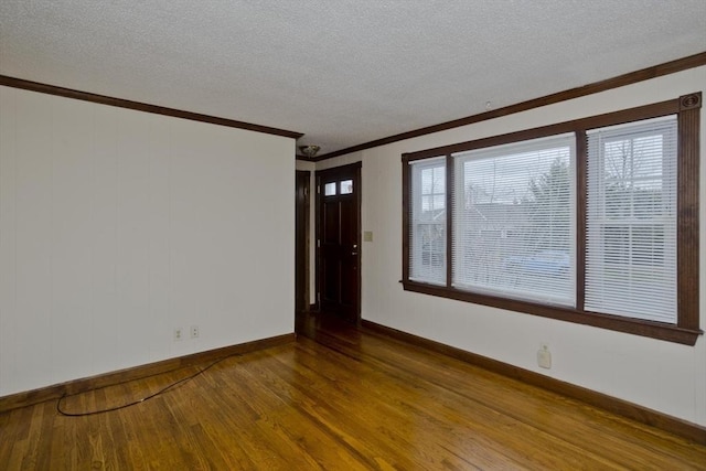spare room with ornamental molding, baseboards, wood finished floors, and a textured ceiling