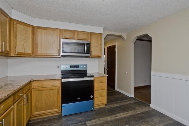 kitchen with dark wood-style flooring, a textured ceiling, backsplash, appliances with stainless steel finishes, and arched walkways