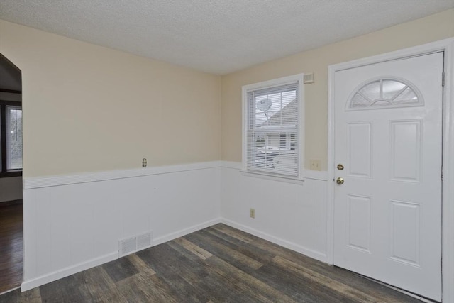 entrance foyer with a textured ceiling, dark wood finished floors, visible vents, and a wainscoted wall
