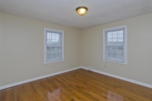 spare room featuring baseboards, a textured ceiling, and wood finished floors