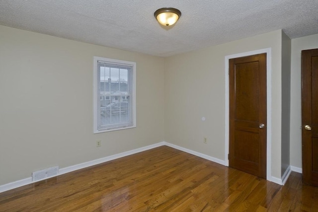 empty room with a textured ceiling, wood finished floors, baseboards, and visible vents