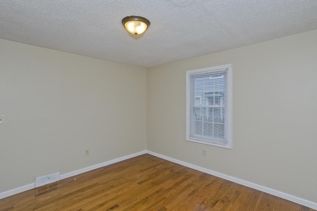 empty room with a textured ceiling, wood finished floors, baseboards, and visible vents