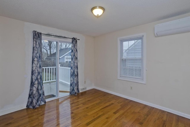 unfurnished room with a healthy amount of sunlight, baseboards, wood finished floors, and a wall unit AC