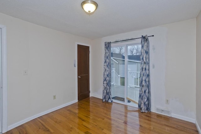 empty room featuring wood finished floors, baseboards, and visible vents