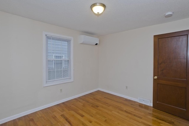 spare room with baseboards, a textured ceiling, visible vents, a wall unit AC, and light wood finished floors