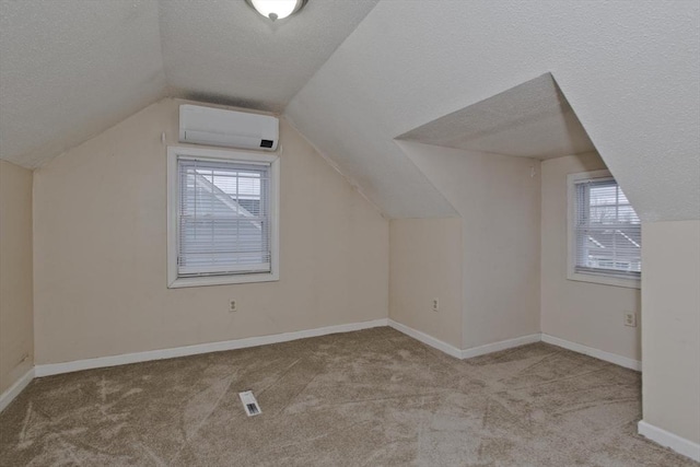 additional living space with an AC wall unit, a healthy amount of sunlight, carpet flooring, and a textured ceiling