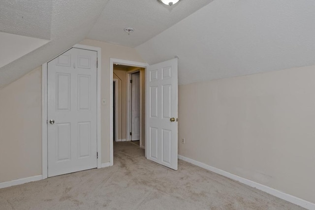 additional living space with baseboards, light colored carpet, vaulted ceiling, and a textured ceiling