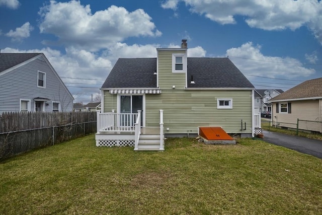 rear view of house with a yard, roof with shingles, fence, and a chimney