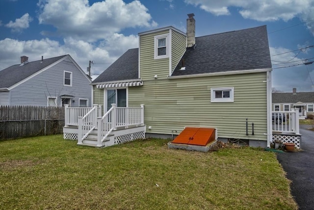 rear view of house featuring a chimney, a wooden deck, a yard, fence, and a shingled roof