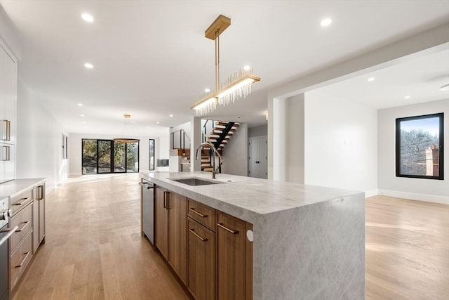 kitchen featuring dishwasher, decorative light fixtures, light hardwood / wood-style floors, sink, and a large island