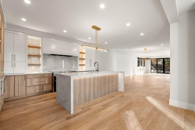 kitchen featuring a large island with sink, pendant lighting, decorative backsplash, sink, and white cabinets