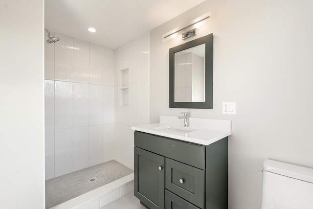 bathroom with toilet, tiled shower, and vanity