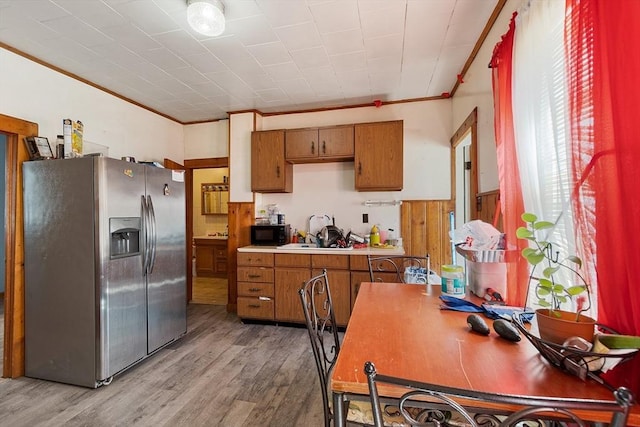 kitchen featuring black microwave, brown cabinets, light wood-type flooring, and stainless steel fridge with ice dispenser